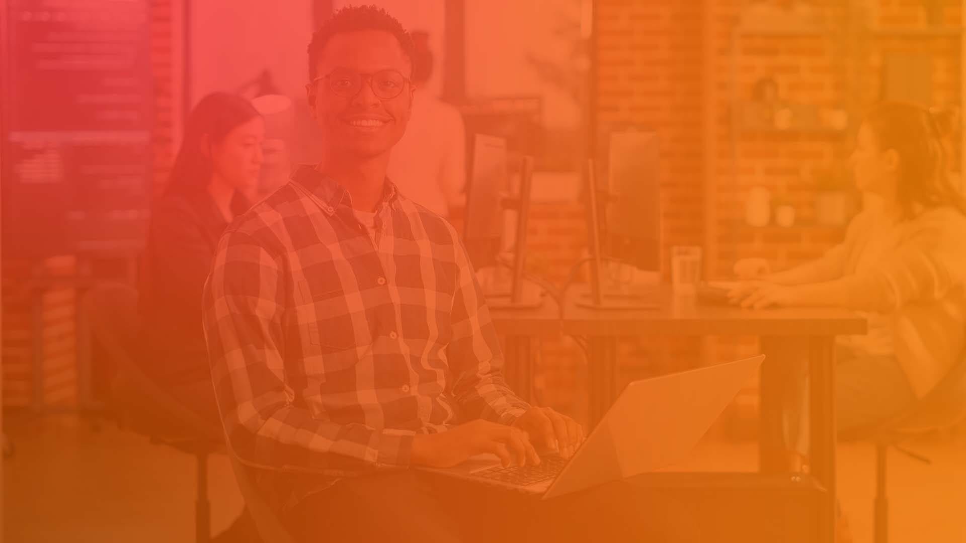 Portrait of artificial intelligence app developer sitting down typing on laptop fixing glasses looking up and smiling