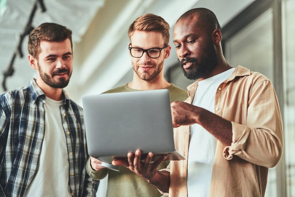 Three multiracial male colleagues looking at laptop screen