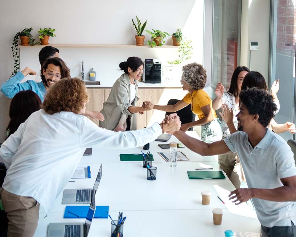 Group of multiracial coworkers shaking hands and hugging to celebrate a new client win for IT company