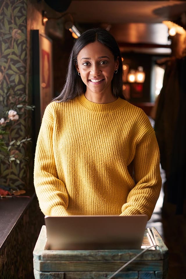 Portrait Of Female Receptionist Working On Laptop At Hotel Check In